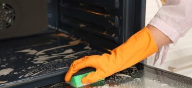 Woman,Cleaning,Oven,Door,With,Sponge,In,Kitchen,,Closeup